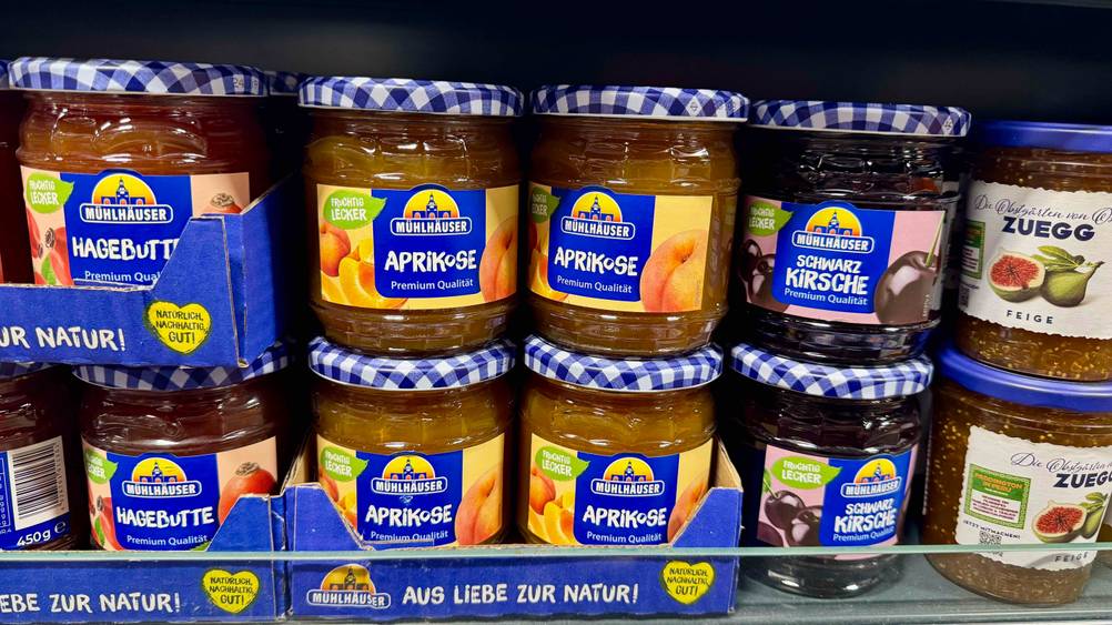Mehrere Gläser der Aprikosenmarmelade im Test stehen neben anderen Produkten in einem Regal.