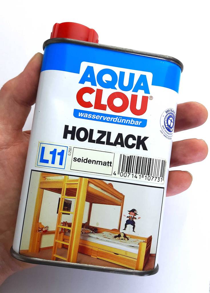 Eine Hand hält den wasserverdünnbaren, getesteten Holz-Klarlack in der 250-ml-Dose vor einer weißen Oberfläche.