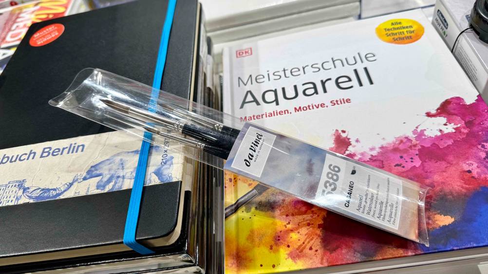 Eine Packung der getesteten Aquarellpinsel liegen auf einem Buch über Aquarell.