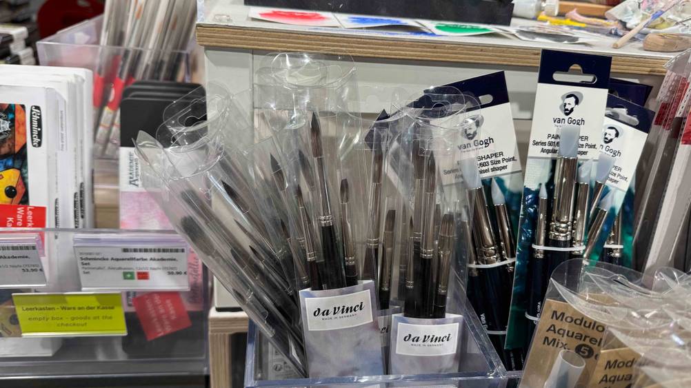 Mehrere Aquarellpinsel im Test in einer Box neben anderen Produkten.