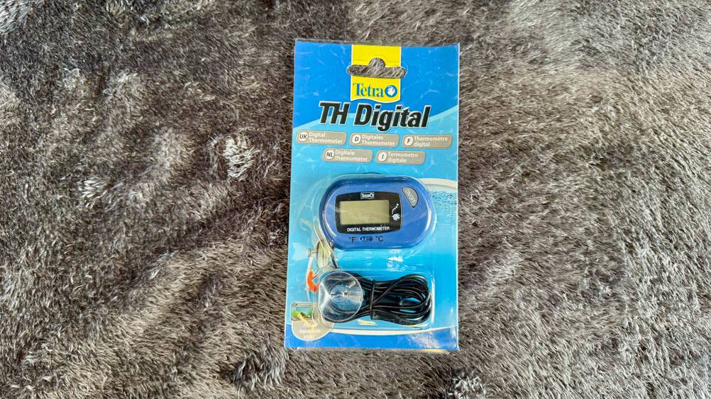 Auf einem grauen Fell liegt das getestete Aquarium-Thermometer.