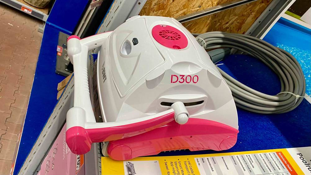 Ein getesteter Poolroboter von der Seite in einem Verkaufsregal dahinter liegt eingerollt sein Kabel.