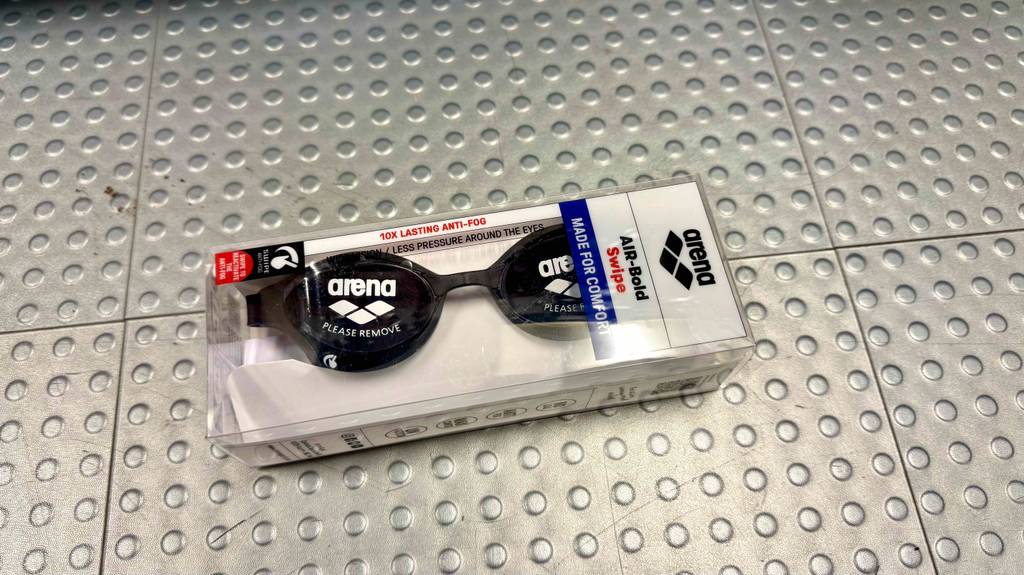 Im Test: Detailansicht einer auf dem Boden liegenden Arena-Schwimmbrille durch die transparente Verpackung.