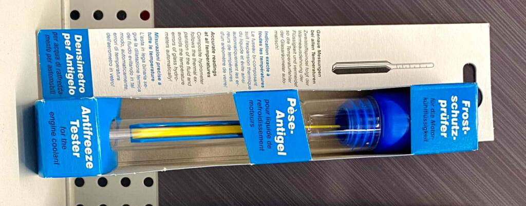 Zwei blaue Originalverpackungen Frostschutzprüfer im Test lehnen an einer braunen Wand in einem Verkaufsbereich.