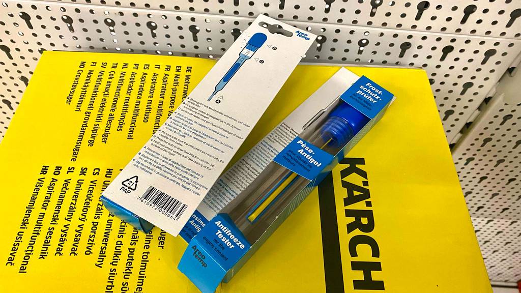 Zwei blaue Verpackungen mit getestetem Frostschutzprüfer und Anwendungsbeschreibung liegen nebeneinander auf einem gelben Karton.