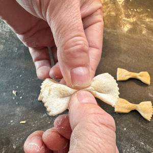 Eine Hand drückt Farfalle aus der Ariete Pastamatic 1593 zusammen