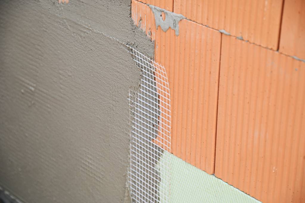 Armierungsgewebe im Test: Eine Wand aus Ziegel und einem anderen Material ist teilweise mit einer dünnen Mörtelschicht und Armierungsgewebe versehen.