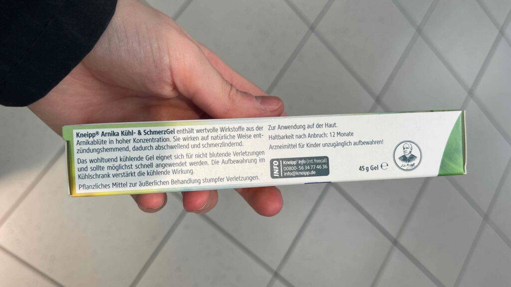 Arnika-Gele-Test: Eine Hand hält die Verpackung des Gels, im Fokus liegt das Gedruckte der Anwendungsbeschreibung.