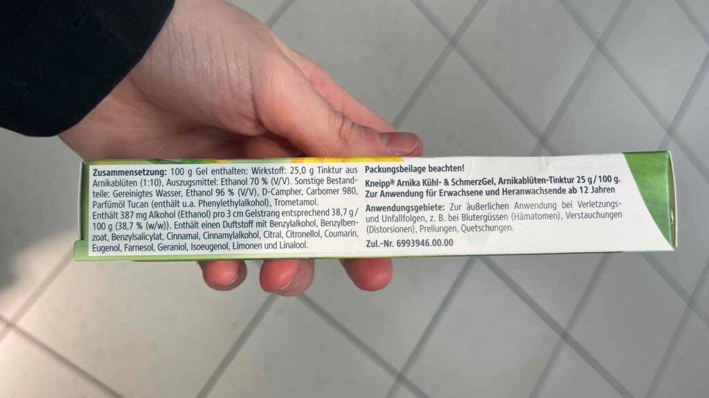 Arnika-Gele im Test: Eine Hand hält die Verpackung des Gels, im Fokus liegt das Gedruckte der Zusammensetzung.