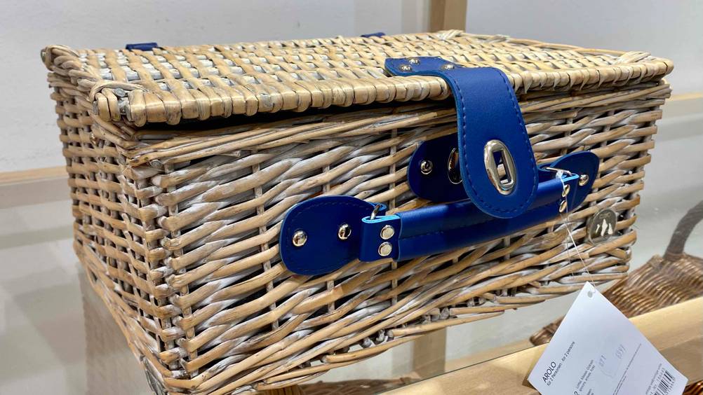 Im Test: Ein Picknickkorb im Rattandesign und blauem Griff steht auf einer Glasoberfläche.