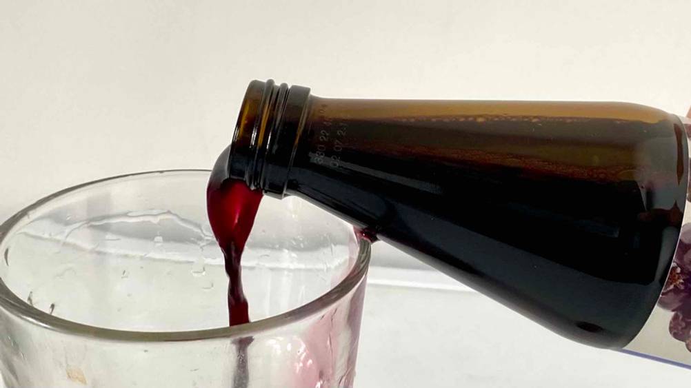 Eingießendes Glas mit Aroniasaft.