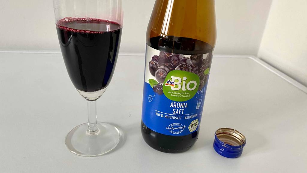 Eine Flasche Aroniasaft neben einem Glas mit Aroniasaft.