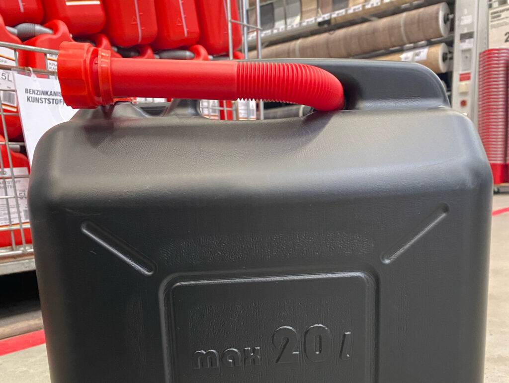 Ein schwarzer Benzinkanister im Test mit rotem Einfüll-Aufsatz für 20 Liter Flüssigkeit steht in einem Verkaufsbereich.