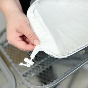 Die Unterseite des Premium Bügeltischbezugs ist sichtbar. Eine Hand hält den Stoff und zeigt den eingezogenen Kordelstopper.