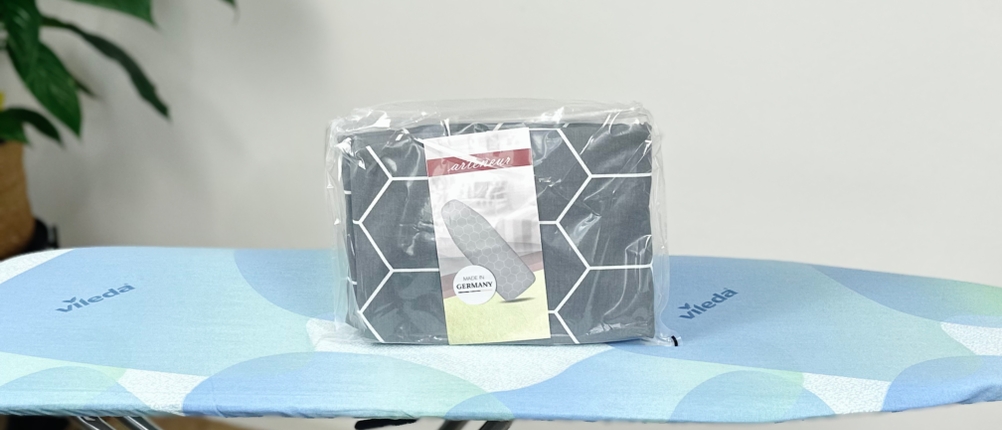 Der arteneur Premium Bügeltischbezug steht in Originalverpackung auf einem blauen Bügelbrett.