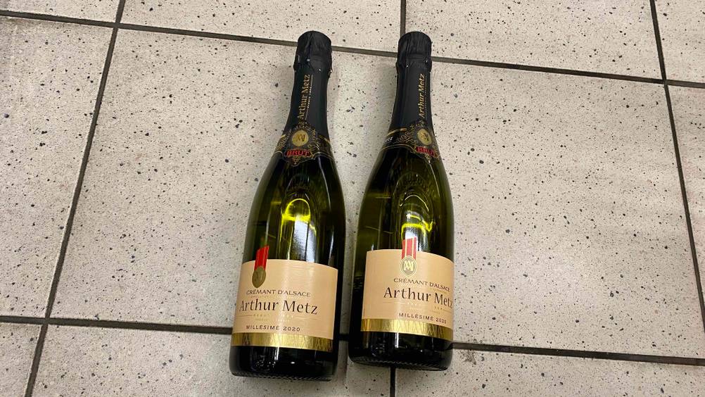 Zwei getestete Flaschen Crémant d’Alsace von Arthur Metz liegen auf dem Boden.