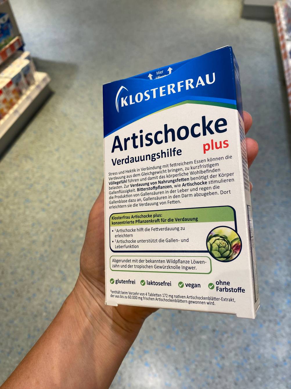 Eine Hand hält die Packung der getesteten Artischocken-Kapseln mit der Rückseite nach vorne.