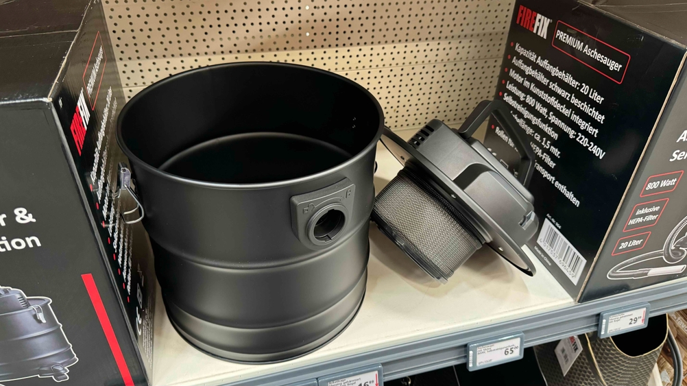 Ein getesteter Aschesauger mit seinem Deckel daneben in einem Verkaufsregal zwischen Katonagen.