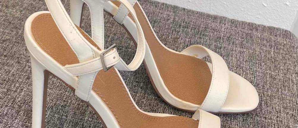 Hochzeitsschuhe-Test: Seitenansicht auf ein Paar offener Schuhe in Creme, die auf einem grauen Stoff vor einer weißen Wand stehen.