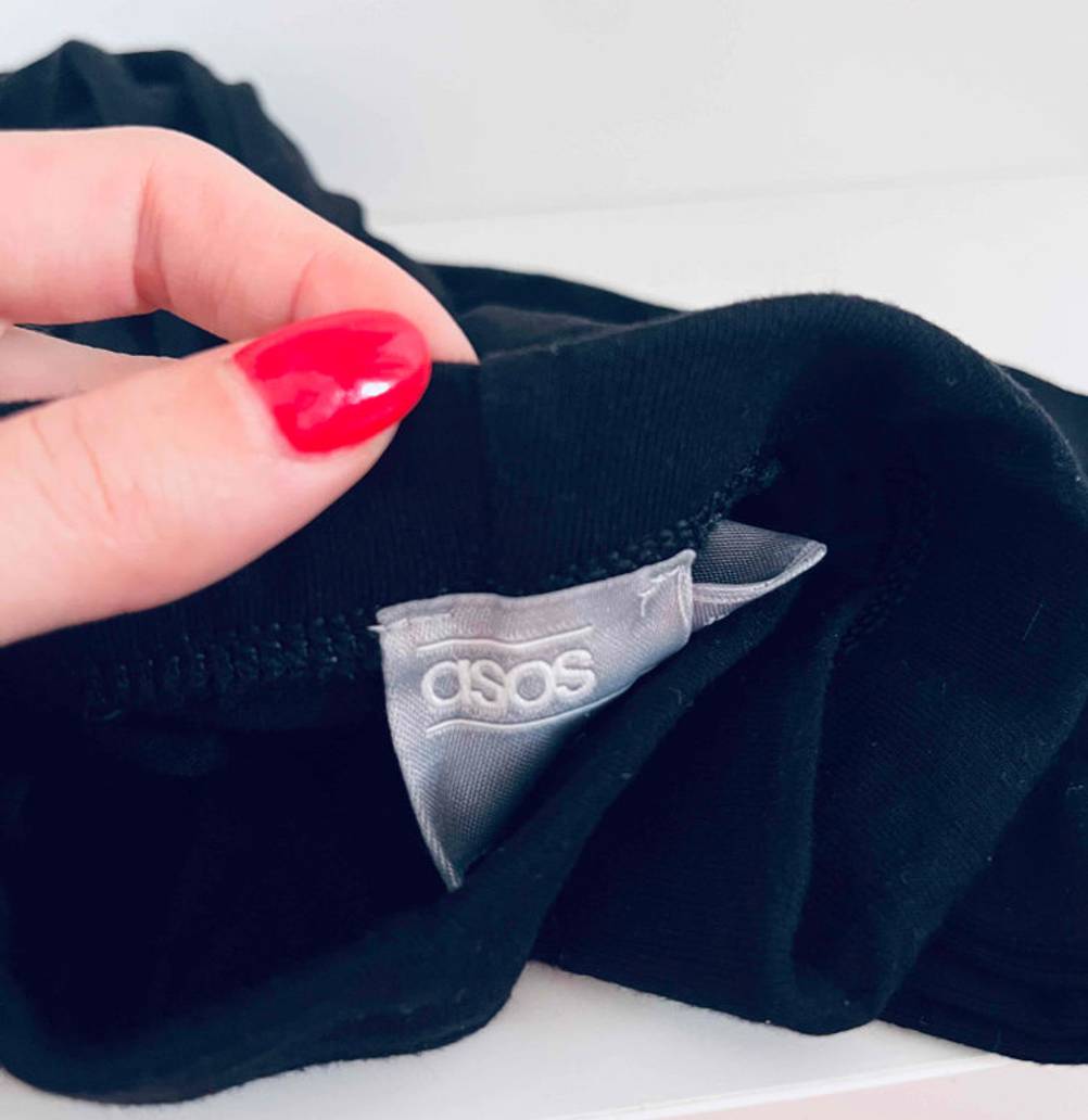 Hand hält schwarze, lange Unterhosen für Damen im Test, mit Blick auf das am Bündchen eingenähte Markenzeichen Asos.