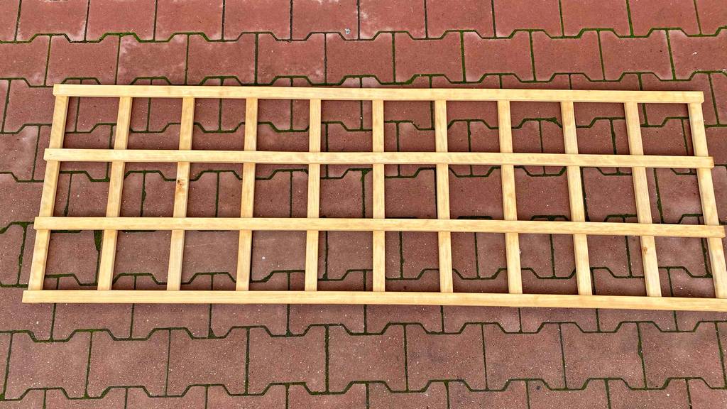 Getestet: Ein Rankgitter aus Holz liegt quer auf einem Pflastersteinboden.