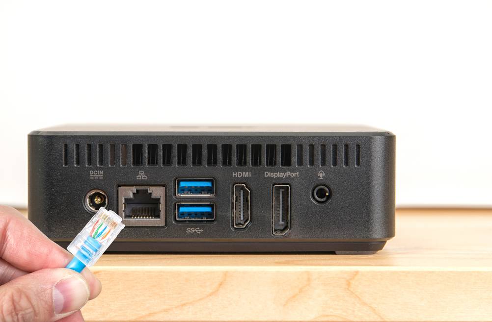 Lüfterlose Mini-PCs im Test: Ein Mann hält ein Netzwerkkabel vor einem Mini-PC.