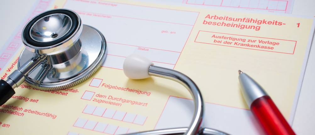Nadeldrucker im Test: Auszufüllende Arbeitsunfähigkeitsbescheinigung und Rezept sowie ein Stethoskop und Kugelschreiber liegen auf einem Schreibtisch.