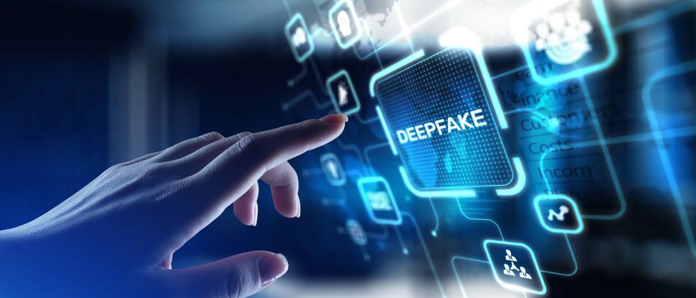Audio-AI im Test: Eine Hand tippt auf einen holografischen Bildschirm mit der Aufschrift „Deepfake“. Im Hintergrund sind Datenpunkte und Netzwerkgrafiken sichtbar.