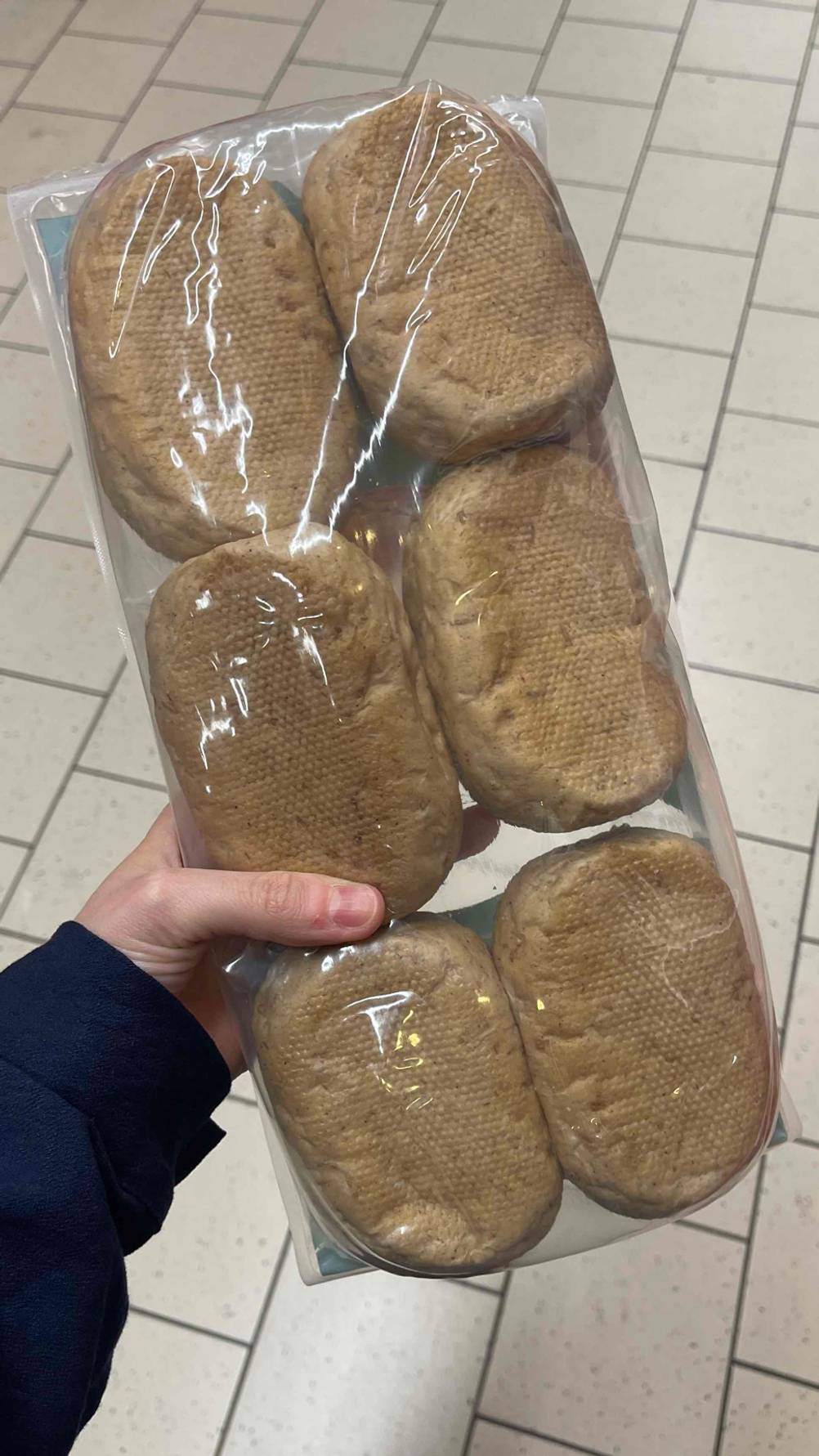 Eine Hand hält die getesteten Aufbackbrötchen in einer Kunststoffpackung über einem Fliesenboden.