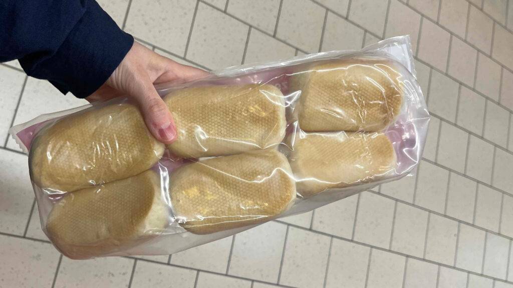 Die transparente Kunststoffverpackung mit sechs hellen Aufbackbrötchen im Test liegt in einer Hand.