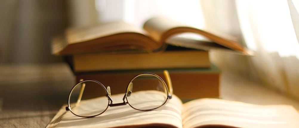 Brille liegt auf aufgeschlagenem Buch.
