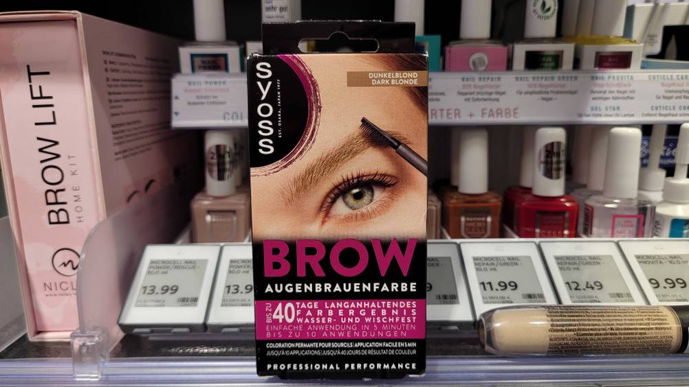 Eine Packung der Augenbrauenfarbe im Test vor einem Regal mit Nagellack stehend.