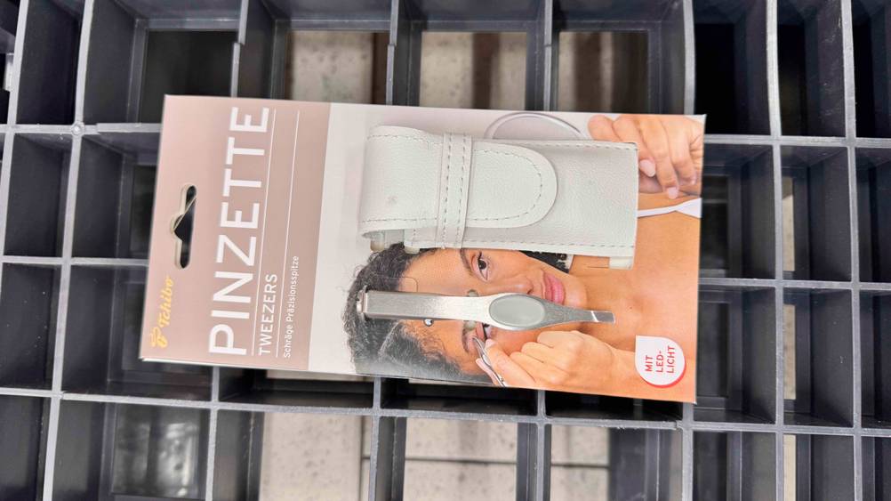Augenbrauenpinzette im Test: Ein Pinzette in Originalverpackung auf einem Gitter.