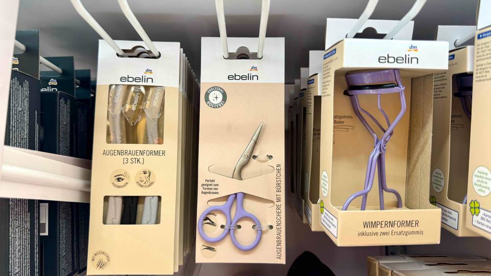 Augenbrauenschere im Test: Mehrere verpackte Scheren hängen in einem Regal zwischen anderen Produkten.