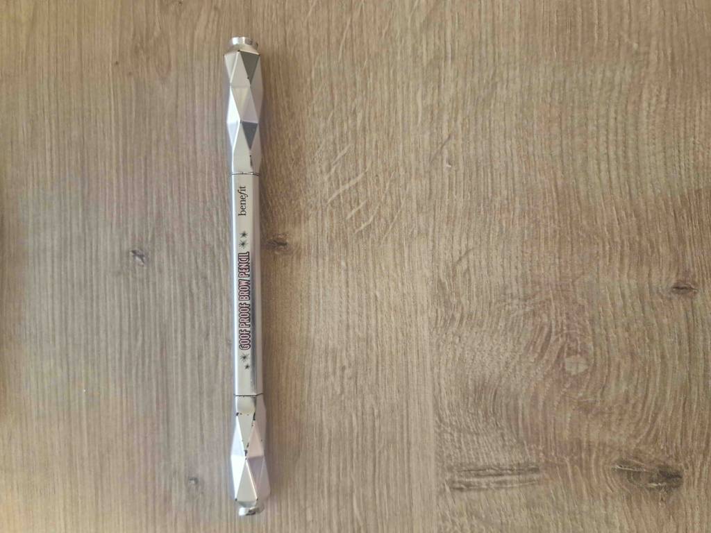 Ein getesteter Augenbrauenstift vertikal auf einer Holzfläche liegend.