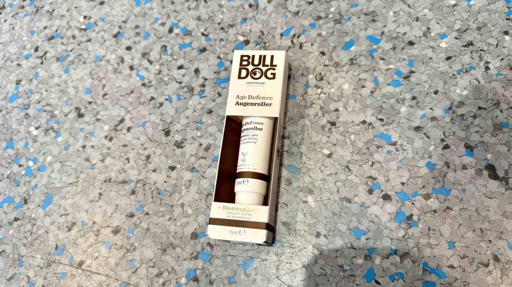 Die getestete Augencreme für Männer liegt auf einem grau-blauen Boden.