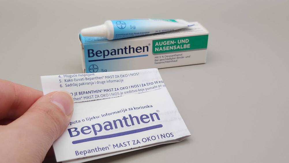 Eine Hand hält den Beipackzettel der getesteten Augensalbe, im Hintergrund eine Tube auf der Verpackung.