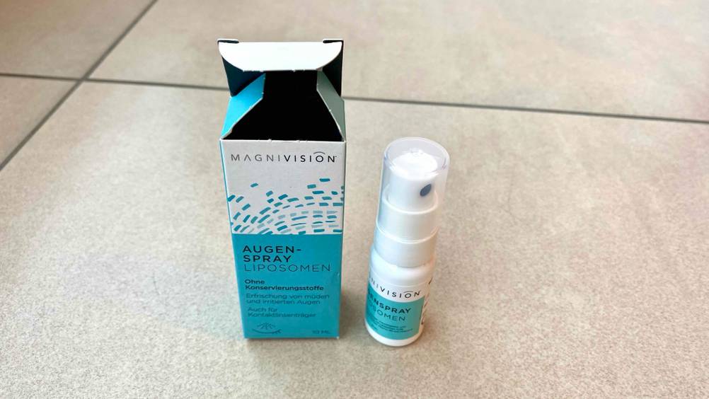 Ein getestetes Augenspray neben seiner Verpackung von schräg oben auf Fließen.