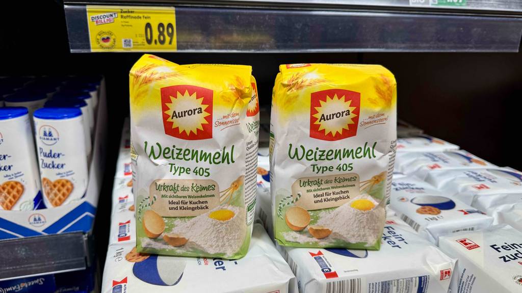 Zwei Packungen mit getestetem Weizenmehl 405 der Marke Aurora stehen in einem Verkaufsregal auf Zuckerpackungen.