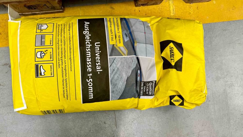 Eine Packung der getesteten Ausgleichsmasse liegt horizontal auf einem Betonboden.