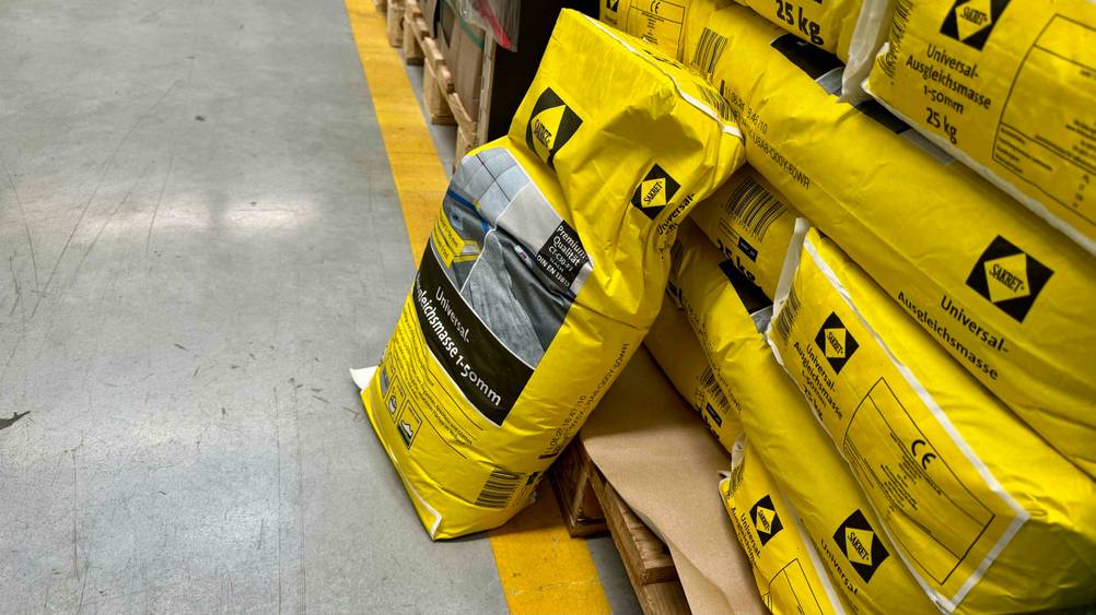 Ausgleichsmasse getestet: Ein Sack lehnt an einem Stapel Ausgleichsmasse auf einer Holzpalette.