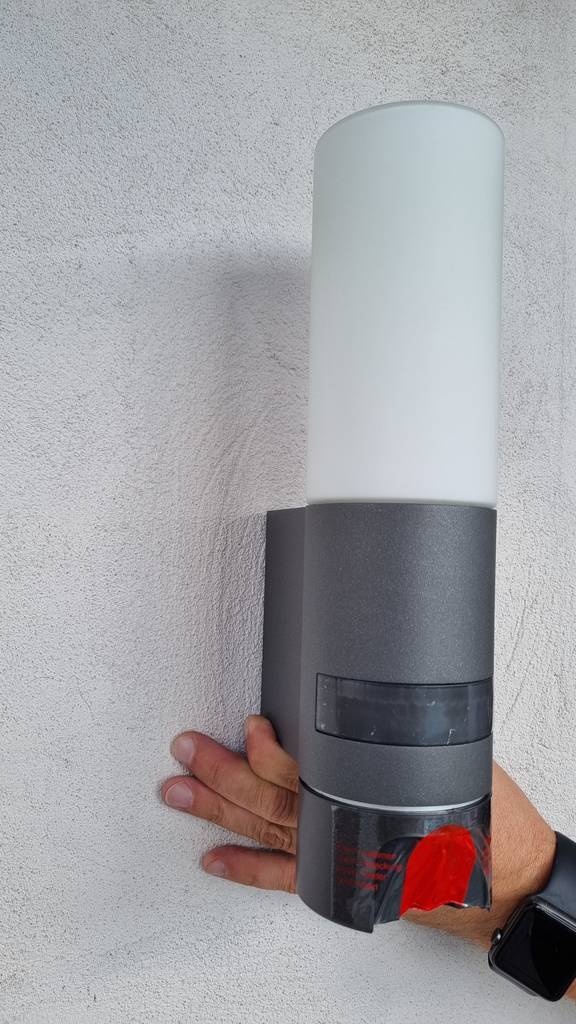 Außenleuchte mit Kamera im Test: Eine Außenleuchte wird von einer Hand an eine Wand gehalten.