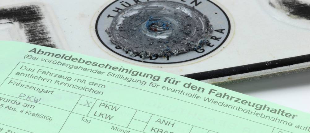 Ein entwertetes Kennzeichen und eine Abmeldebescheinigung liegen auf einem hellen Hintergrund.