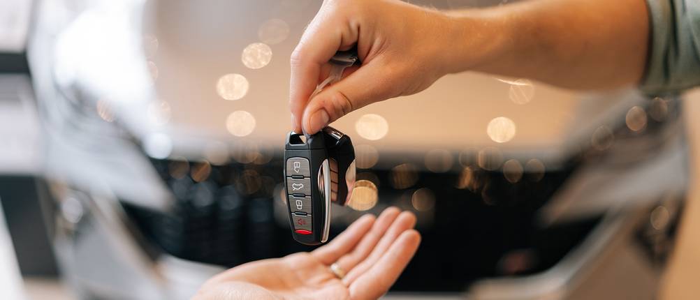 Plattformen zum Auto verkaufen im Test: Ein Verkäufer reicht einem Kunden den Autoschlüssel.