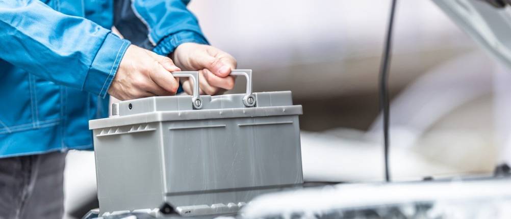50-Ah-Autobatterie-Test: Eine Autobatterie wird an den beiden Griffen gehalten.