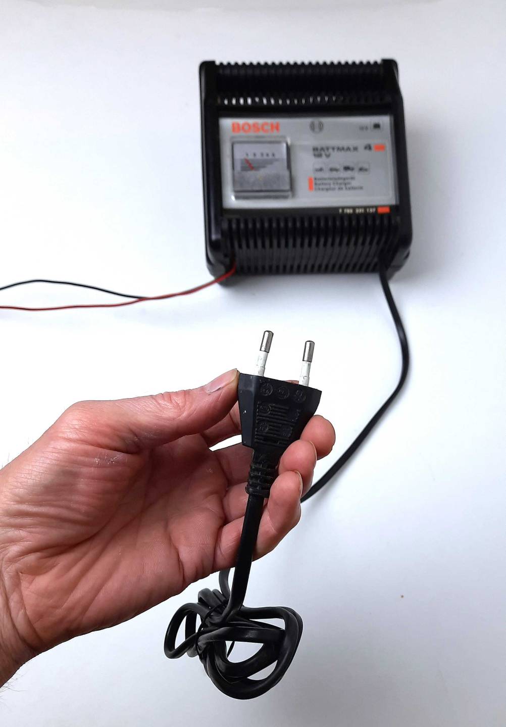 Eine Hand hält den Stecker des getesteten Autobatterie-Ladegerätes, im Hintergrund das Gerät.