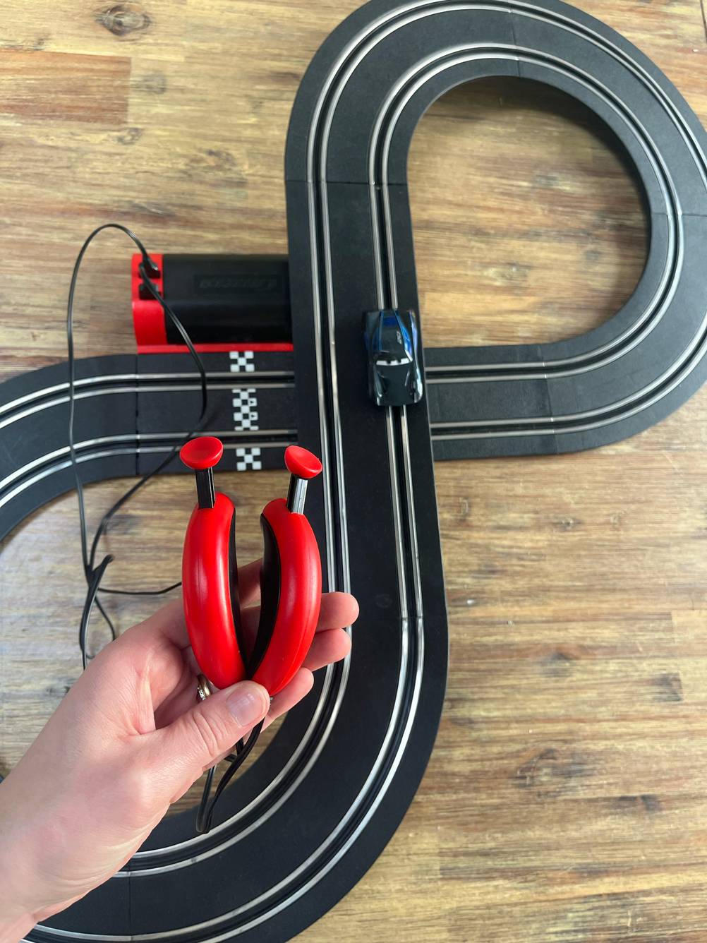 Eine Hand hält die Bedienelemente der Autorennbahn im Test vor die Rennbahn auf dem Boden.