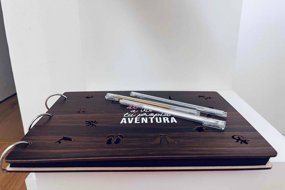 Reisetagebuch-Test: Ein Reisetagebuch von Aventura inklusive Spiralbindung liegt geschlossen auf einem hellen Regal. Darauf befinden sich drei Stifte.