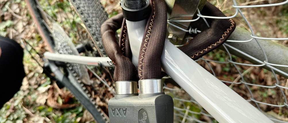 Das abgeschlossene Axa Foldable 600 sichert das Fahrrad an einem Zaun. Die Kettenglieder liegen eng an Rahmen und Pfosten.