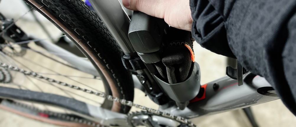 Das Axa Foldable 600 wird aus der Halterung am Fahrradrahmen gezogen. Eine Hand greift das Schloss von oben.